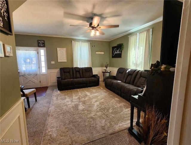 living area with wainscoting, ceiling fan, carpet, crown molding, and a decorative wall