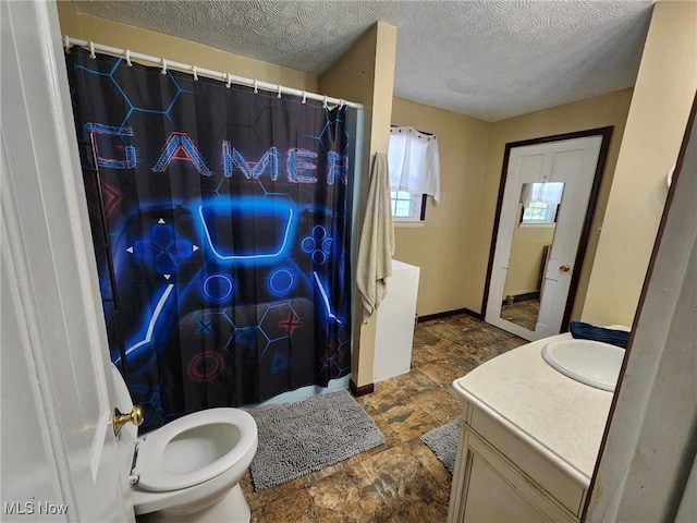 bathroom featuring toilet, stone finish floor, vanity, a textured ceiling, and baseboards