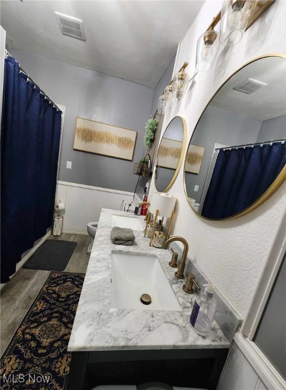 bathroom with toilet, a wainscoted wall, visible vents, and vanity