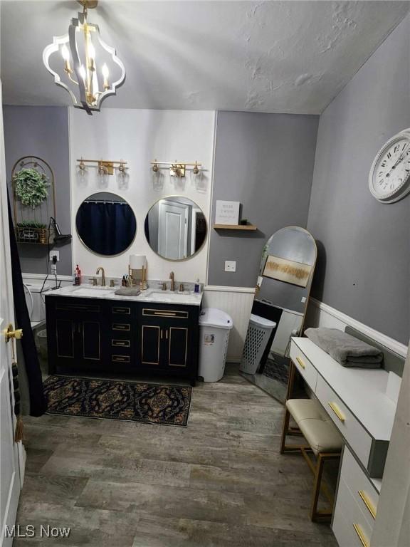 bathroom featuring double vanity, wood finished floors, a sink, and a notable chandelier