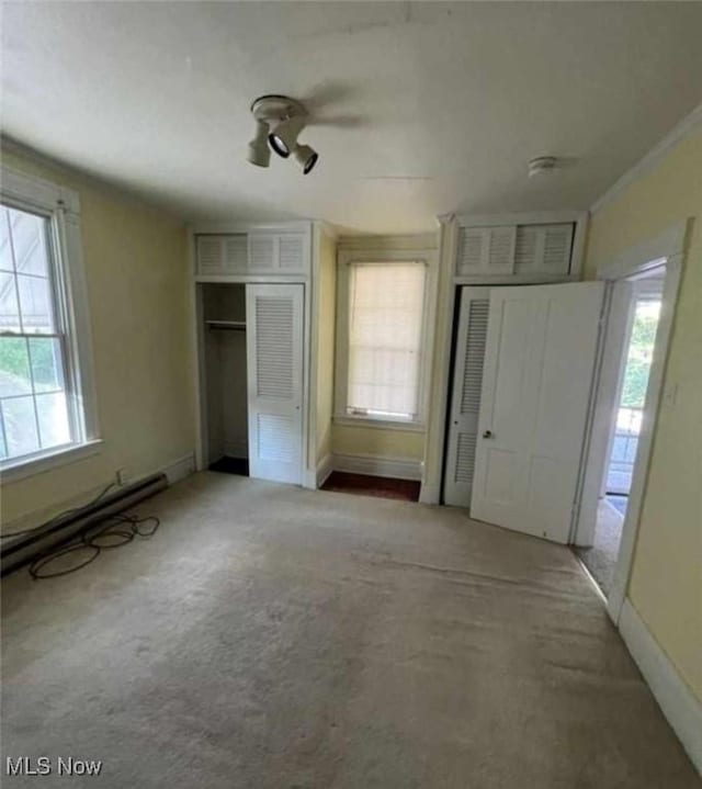 unfurnished bedroom with ceiling fan, baseboard heating, carpet, and multiple closets