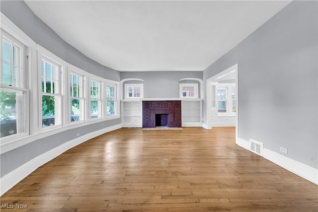 unfurnished living room with light hardwood / wood-style floors, a brick fireplace, and built in features