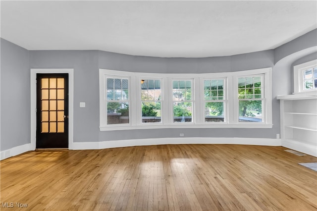 unfurnished living room featuring built in shelves, light hardwood / wood-style flooring, and a healthy amount of sunlight