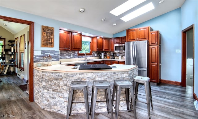 kitchen with dark hardwood / wood-style flooring, tasteful backsplash, lofted ceiling with skylight, a breakfast bar, and appliances with stainless steel finishes