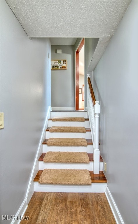 stairway featuring a textured ceiling and wood-type flooring