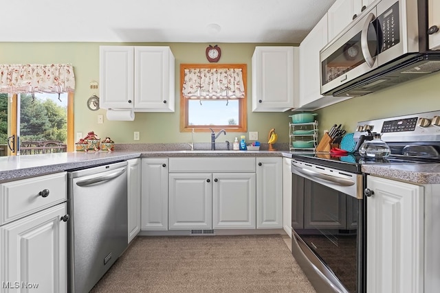 kitchen with white cabinetry, stainless steel appliances, light colored carpet, and a healthy amount of sunlight