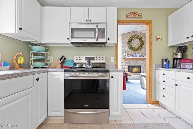 kitchen featuring light tile patterned floors, a textured ceiling, white cabinetry, a fireplace, and stainless steel appliances