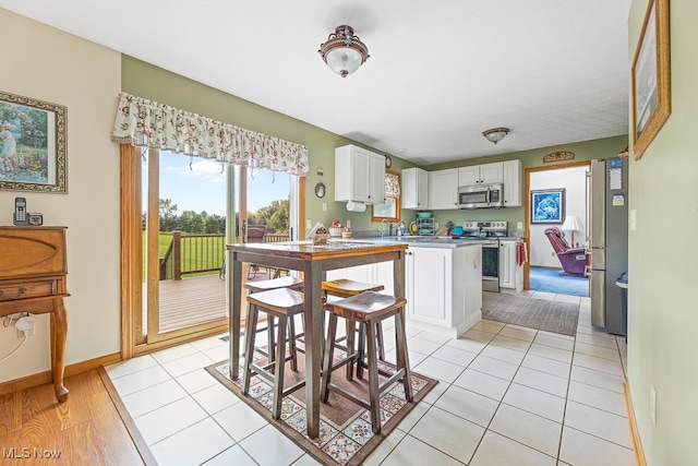 kitchen with a kitchen breakfast bar, white cabinets, stainless steel appliances, and light tile patterned floors