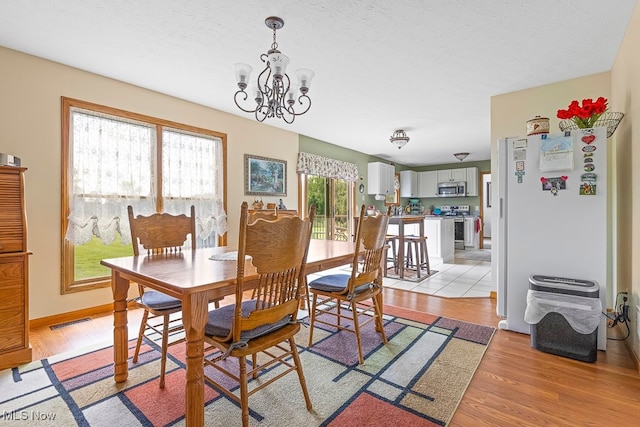 dining space featuring a textured ceiling, light hardwood / wood-style flooring, plenty of natural light, and an inviting chandelier