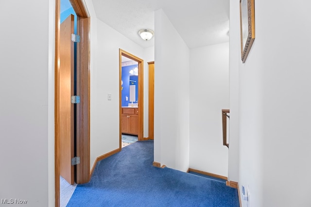 hallway with dark carpet and a textured ceiling