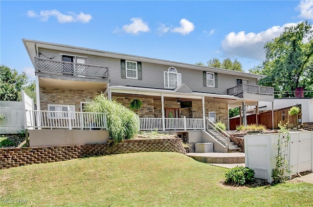 rear view of property with a balcony, ceiling fan, covered porch, and a yard