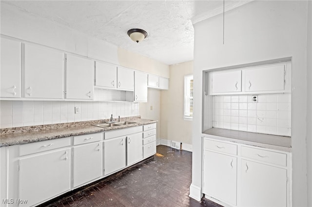 kitchen featuring tasteful backsplash, white cabinetry, a sink, and visible vents