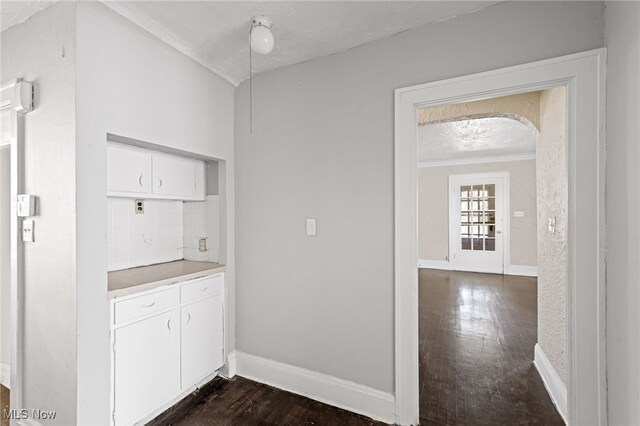 interior space with decorative backsplash, dark hardwood / wood-style floors, crown molding, a textured ceiling, and white cabinets