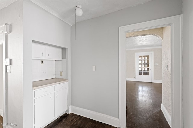 kitchen featuring arched walkways, baseboards, white cabinets, dark wood-style floors, and crown molding