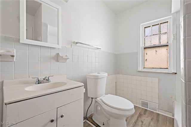 half bath featuring tile walls, visible vents, toilet, vanity, and wood finished floors