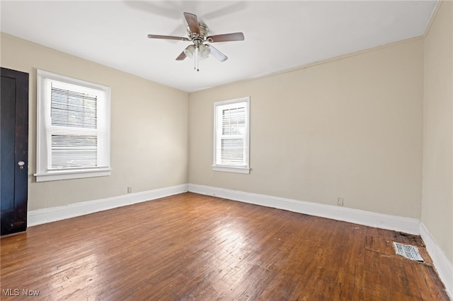 empty room featuring a ceiling fan, wood finished floors, visible vents, and baseboards