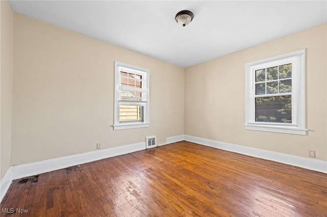 empty room featuring a wealth of natural light, visible vents, hardwood / wood-style floors, and baseboards