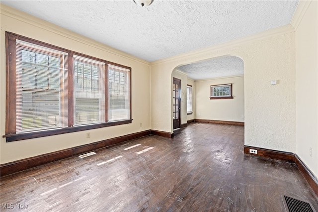 empty room featuring dark wood-style floors, visible vents, arched walkways, and ornamental molding