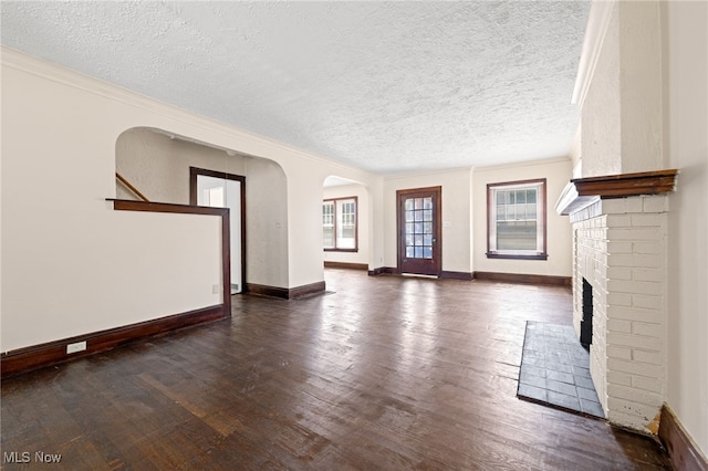 unfurnished living room featuring baseboards, arched walkways, dark wood finished floors, crown molding, and a fireplace