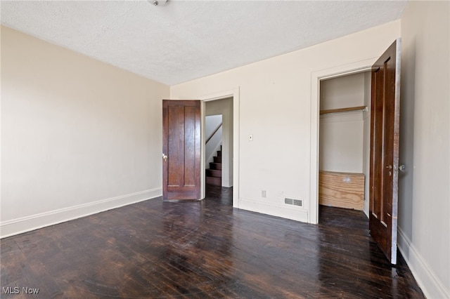 unfurnished bedroom featuring dark wood-type flooring, visible vents, a textured ceiling, and baseboards