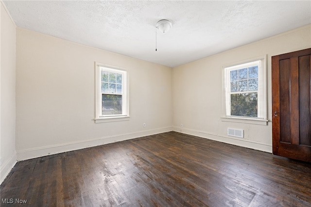 empty room with dark wood-style floors, a textured ceiling, visible vents, and baseboards