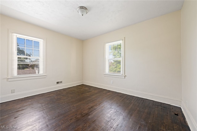 empty room featuring dark wood-style flooring, visible vents, and baseboards