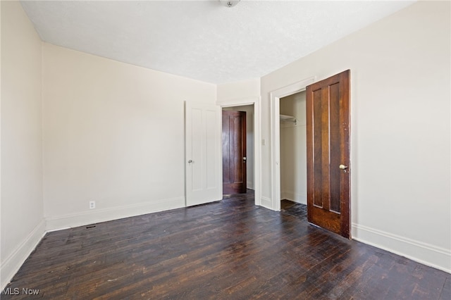 unfurnished bedroom featuring a textured ceiling, a closet, baseboards, and dark wood-type flooring