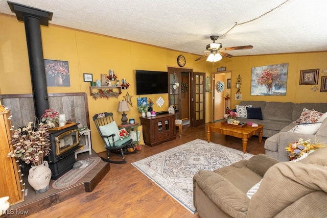 living room with a textured ceiling, wood-type flooring, ceiling fan, and a wood stove