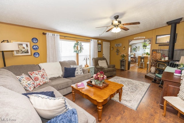 living room featuring lofted ceiling, ceiling fan, a wood stove, and dark hardwood / wood-style floors