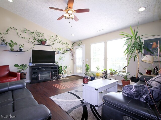 living room featuring ceiling fan, hardwood / wood-style flooring, a fireplace, a textured ceiling, and lofted ceiling