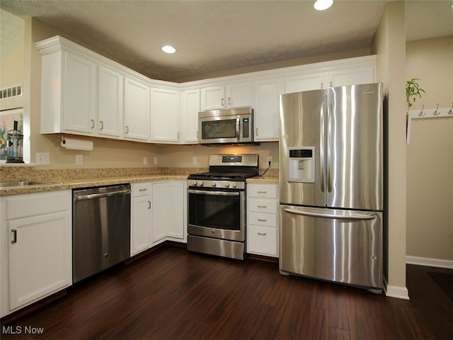 kitchen with appliances with stainless steel finishes, white cabinets, dark hardwood / wood-style floors, and light stone countertops