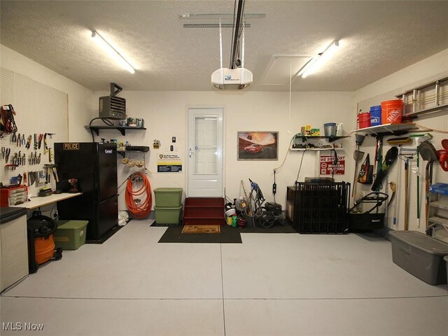 garage with a workshop area, black refrigerator, and a garage door opener