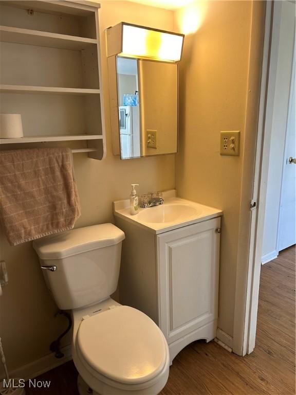 half bathroom with baseboards, toilet, wood finished floors, and vanity