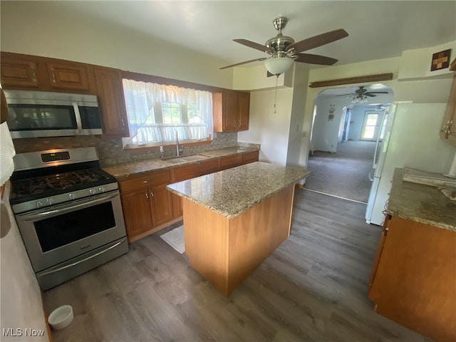 kitchen with stainless steel appliances, sink, dark wood-type flooring, ceiling fan, and a kitchen island