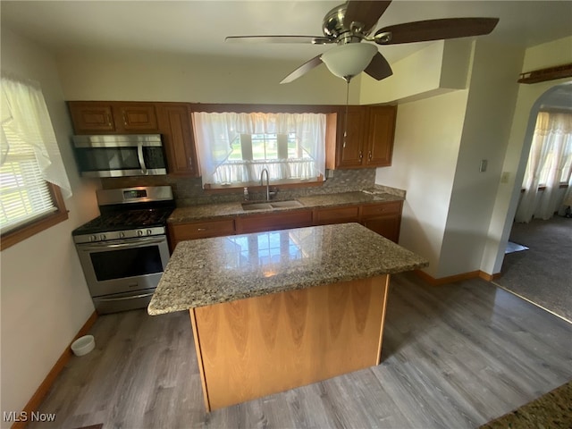 kitchen with a kitchen island, dark hardwood / wood-style floors, stainless steel appliances, sink, and light stone counters