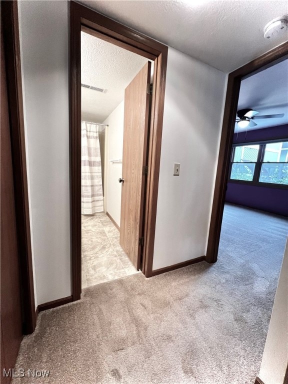 hall with a textured ceiling and light colored carpet