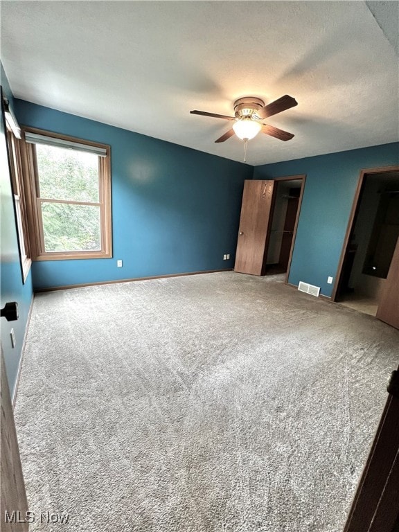 carpeted bedroom featuring a textured ceiling, a walk in closet, a closet, and ceiling fan