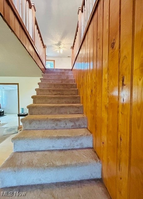 stairs with ceiling fan and wood walls