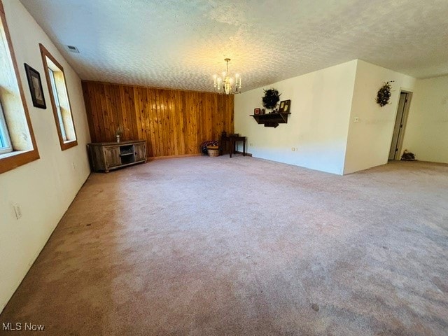 empty room with a notable chandelier, a textured ceiling, and carpet floors