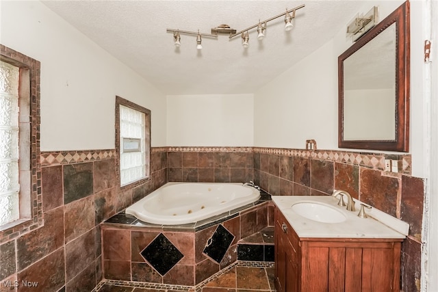 bathroom featuring rail lighting, vanity, tile walls, a textured ceiling, and a relaxing tiled tub