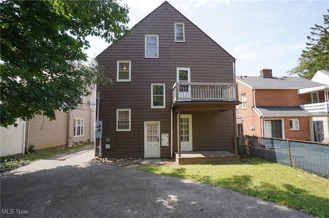 back of property featuring a balcony and a lawn