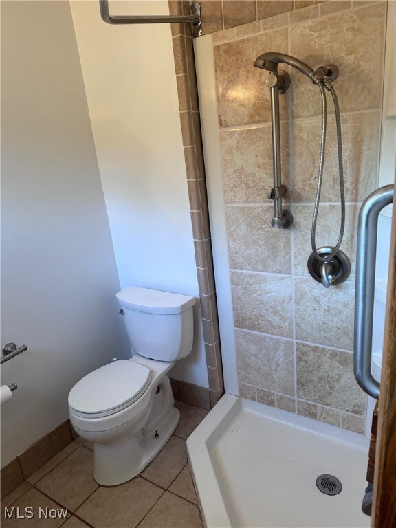 bathroom featuring tiled shower, toilet, and tile patterned flooring