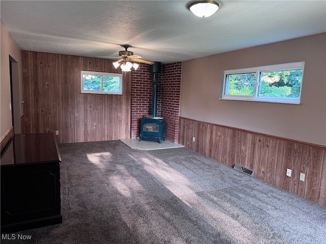 unfurnished living room with ceiling fan, brick wall, carpet, a wood stove, and wood walls