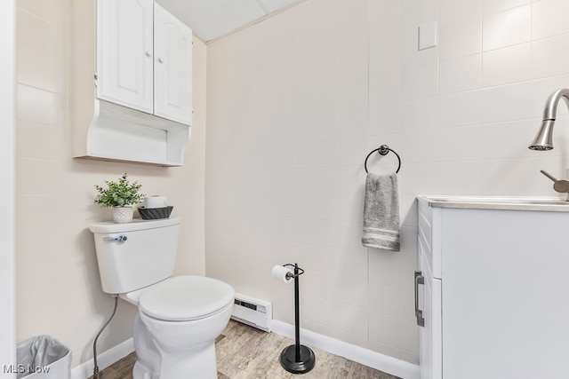 bathroom with tile walls, wood-type flooring, toilet, and a baseboard radiator