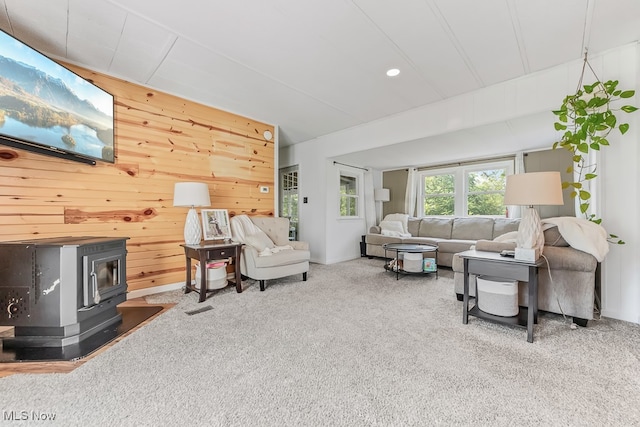 living room featuring a wood stove, carpet flooring, and wooden walls