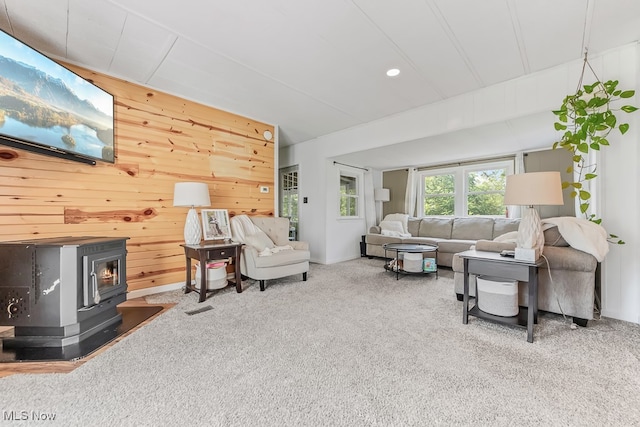 living room featuring a wood stove, carpet flooring, and wood walls