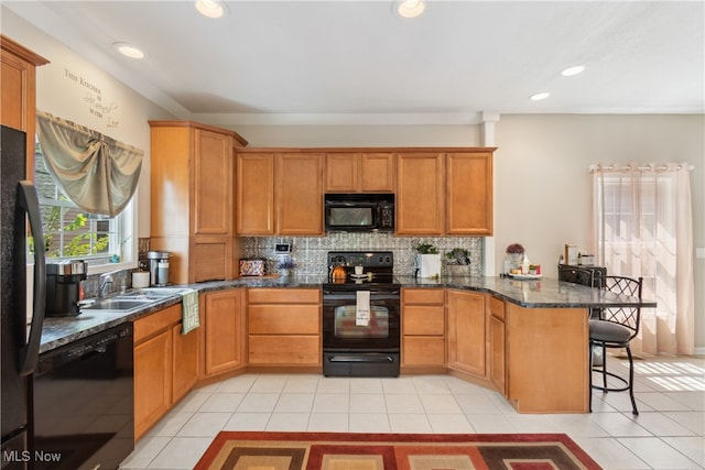 kitchen featuring light tile patterned floors, black appliances, dark stone counters, kitchen peninsula, and a kitchen bar