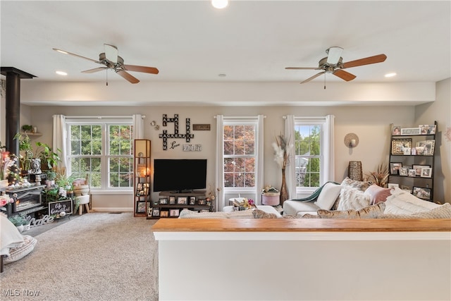 living room with ceiling fan, a wood stove, carpet, and a healthy amount of sunlight