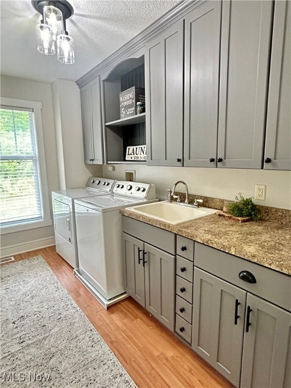 clothes washing area with a textured ceiling, light hardwood / wood-style flooring, cabinets, washer and dryer, and sink