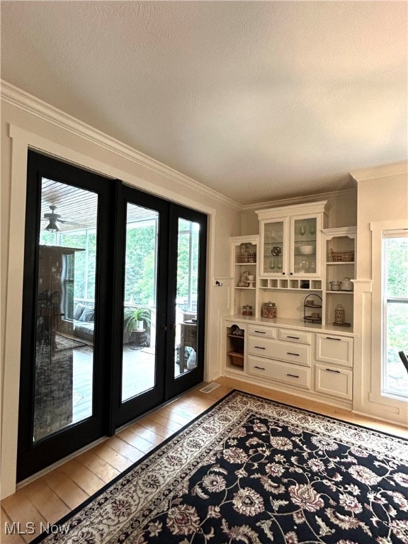 doorway featuring light wood-type flooring, french doors, ornamental molding, and a healthy amount of sunlight